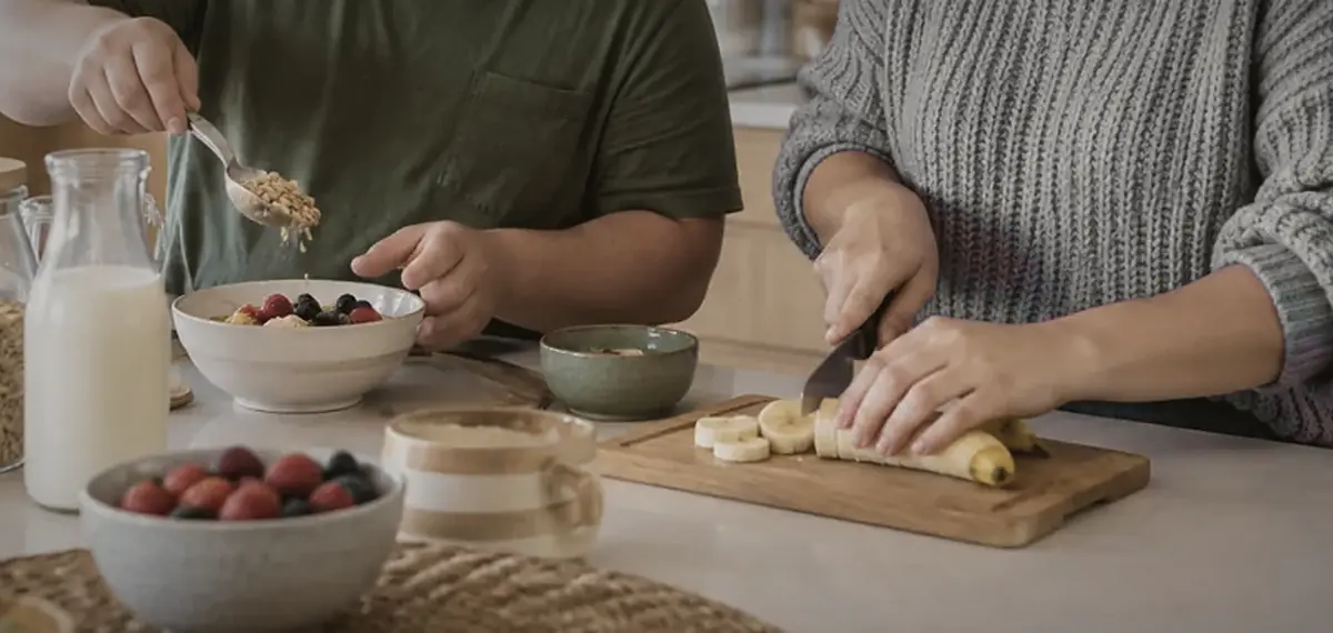Hands preparing breakfast: oats, berries and sliced banana on a chopping board