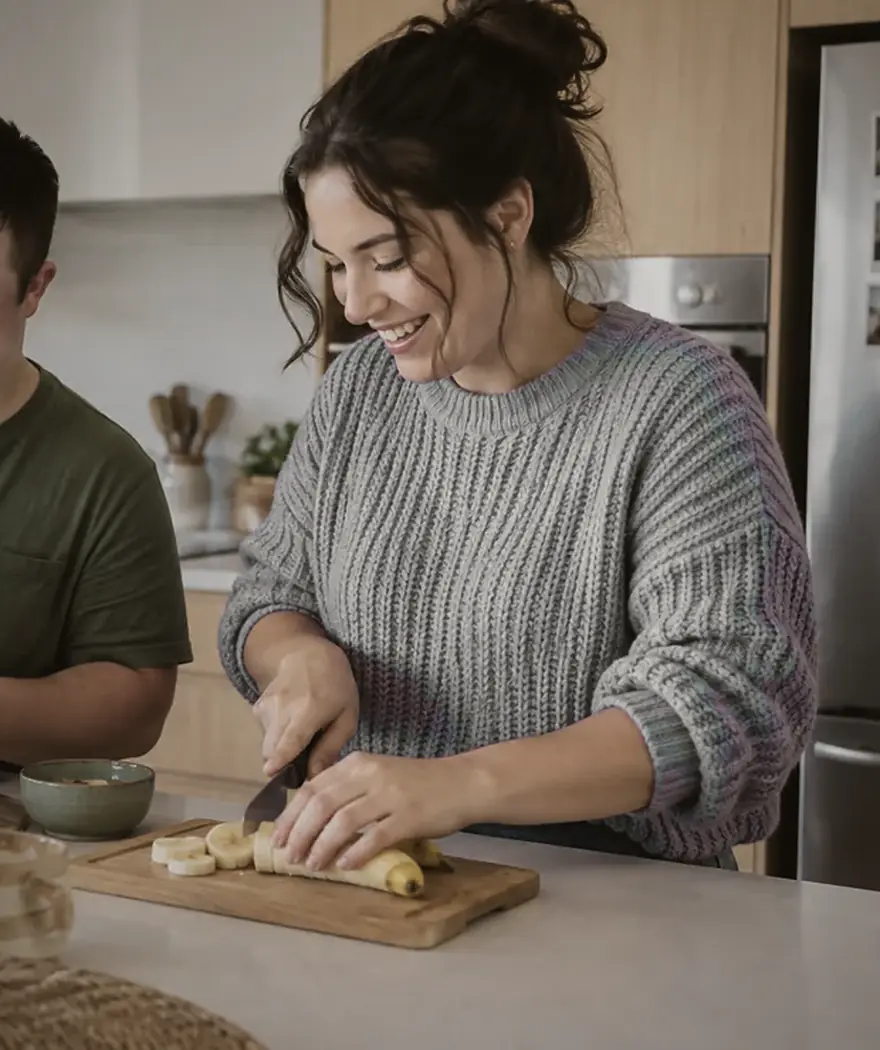 A support worker smiling while slicing banana at a kitchen bench
